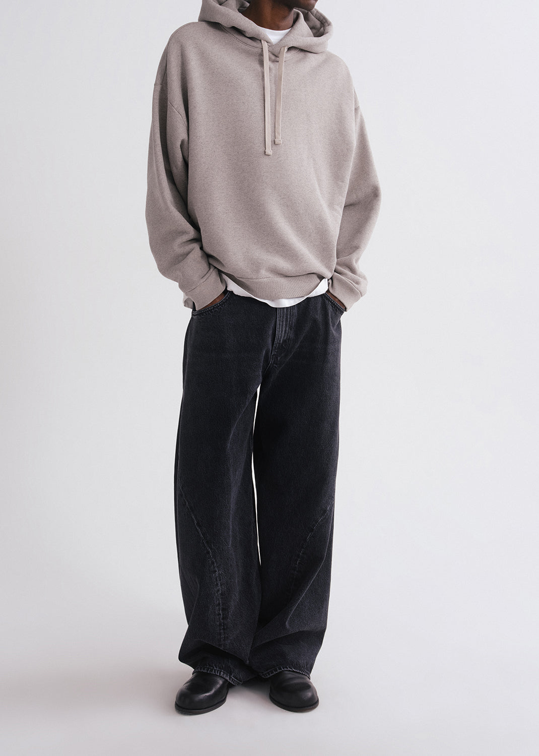 Person wearing grey hoodie, white shirt and black pants on a grey background