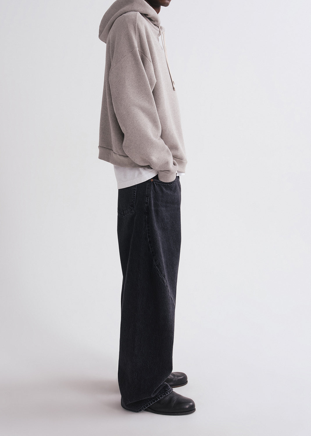 Side of person wearing grey hoodie, white shirt and black pants on a grey background