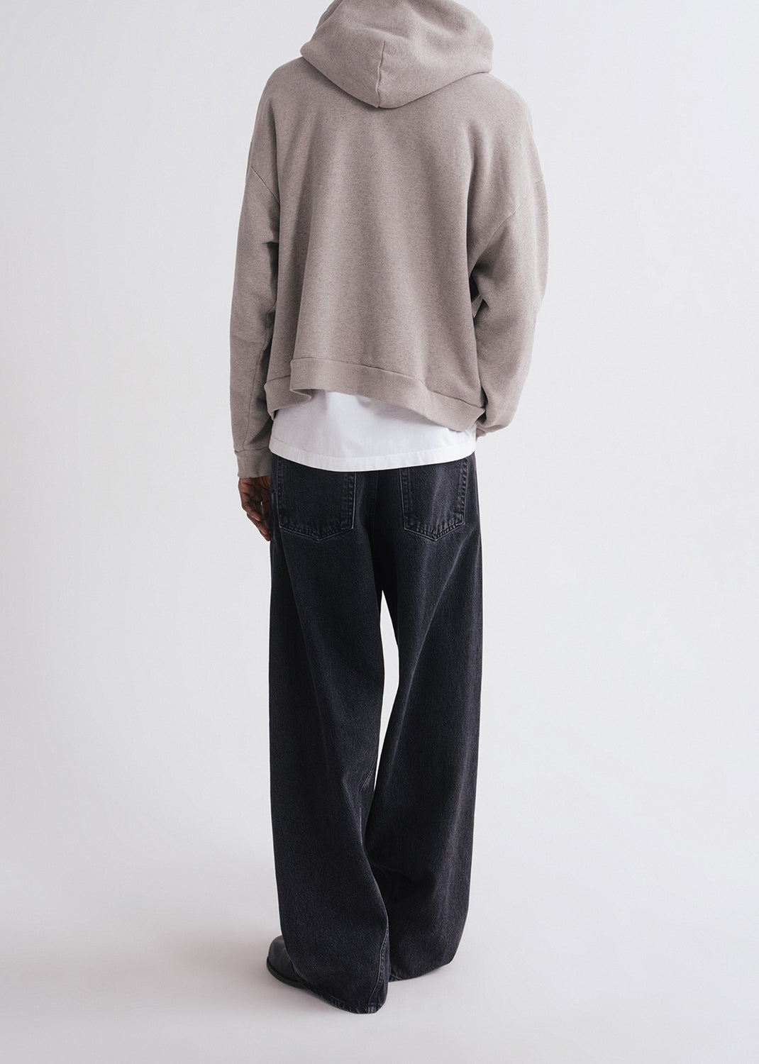Back of person wearing grey hoodie, white shirt and black pants on a grey background