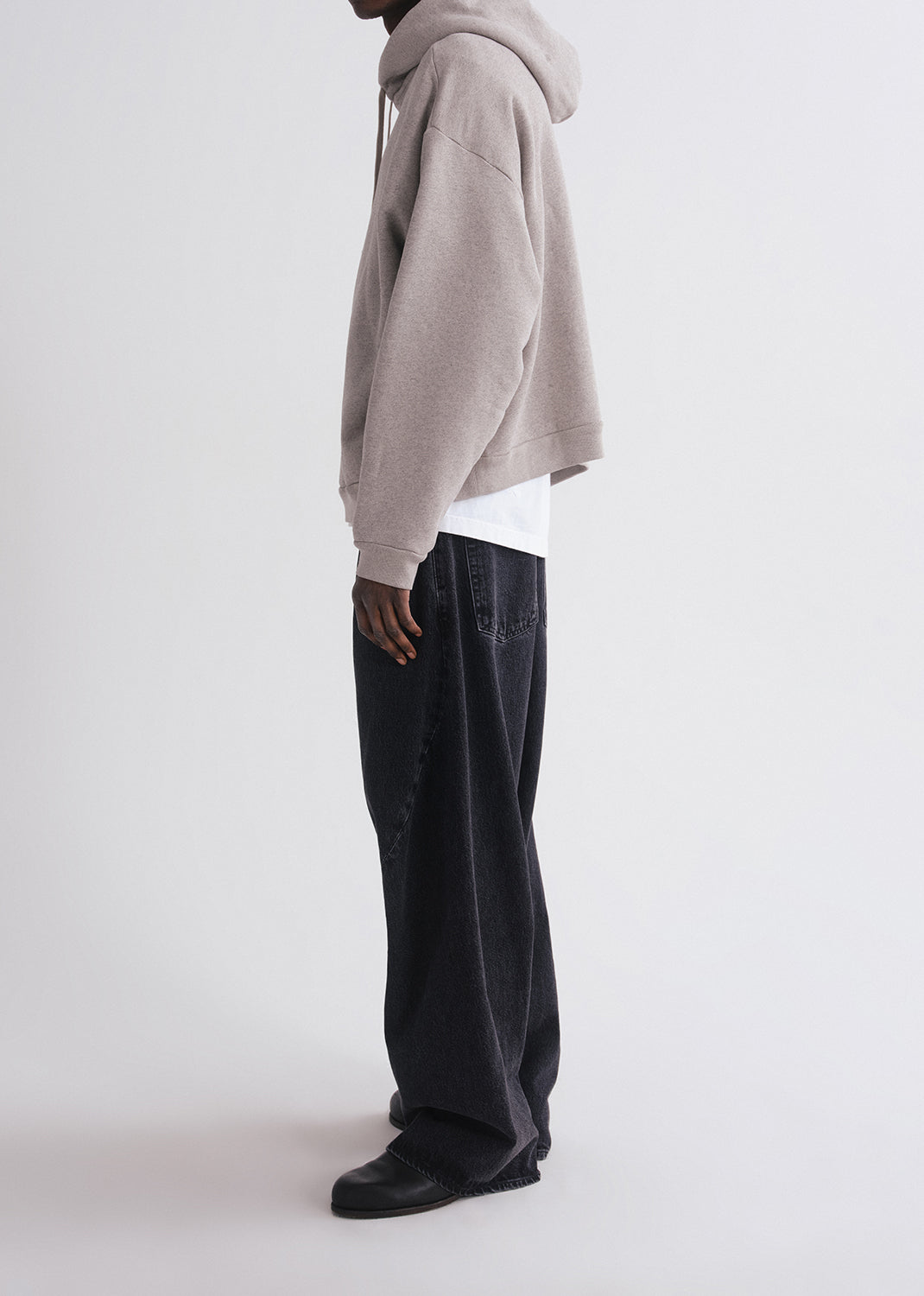 Person wearing grey hoodie, white shirt and black pants on a grey background
