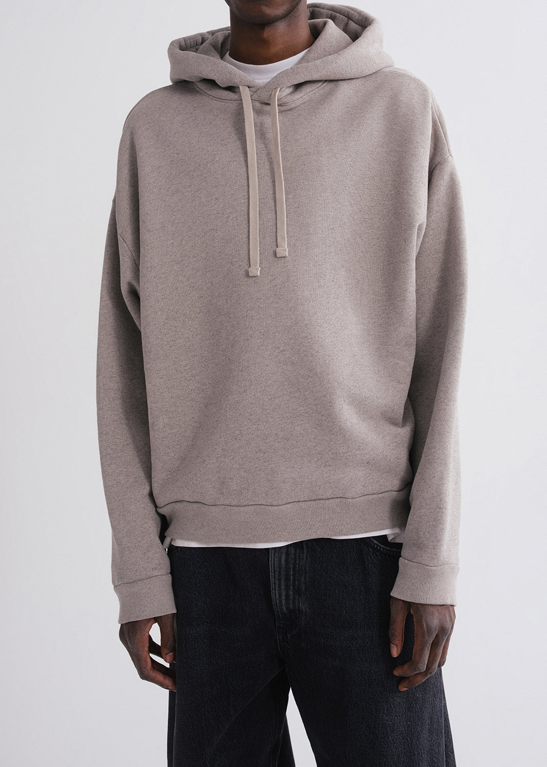 Close up shot of person wearing grey hoodie, white shirt and black pants on a grey background
