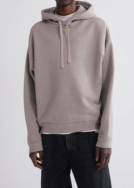 Close up shot of person wearing grey hoodie, white shirt and black pants on a grey background