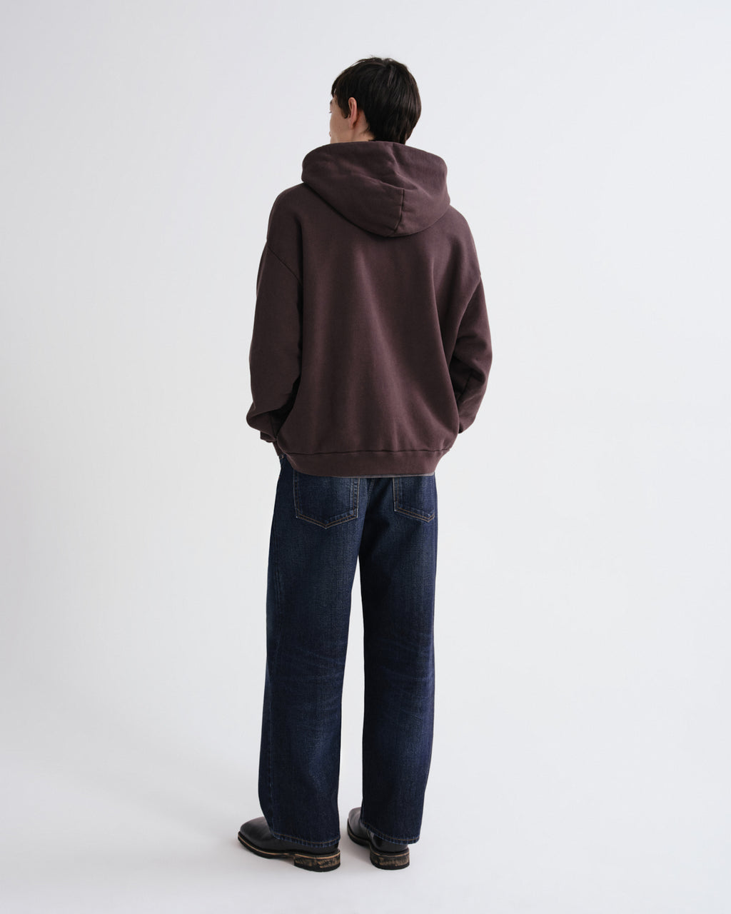Person wearing a brown hoodie and blue jeans on a white background