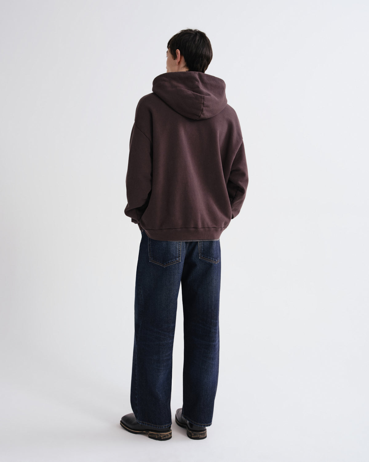 Person wearing a brown hoodie and blue jeans on a white background