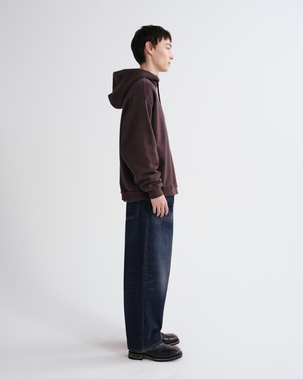 Person wearing a brown hoodie and blue jeans standing against a white background