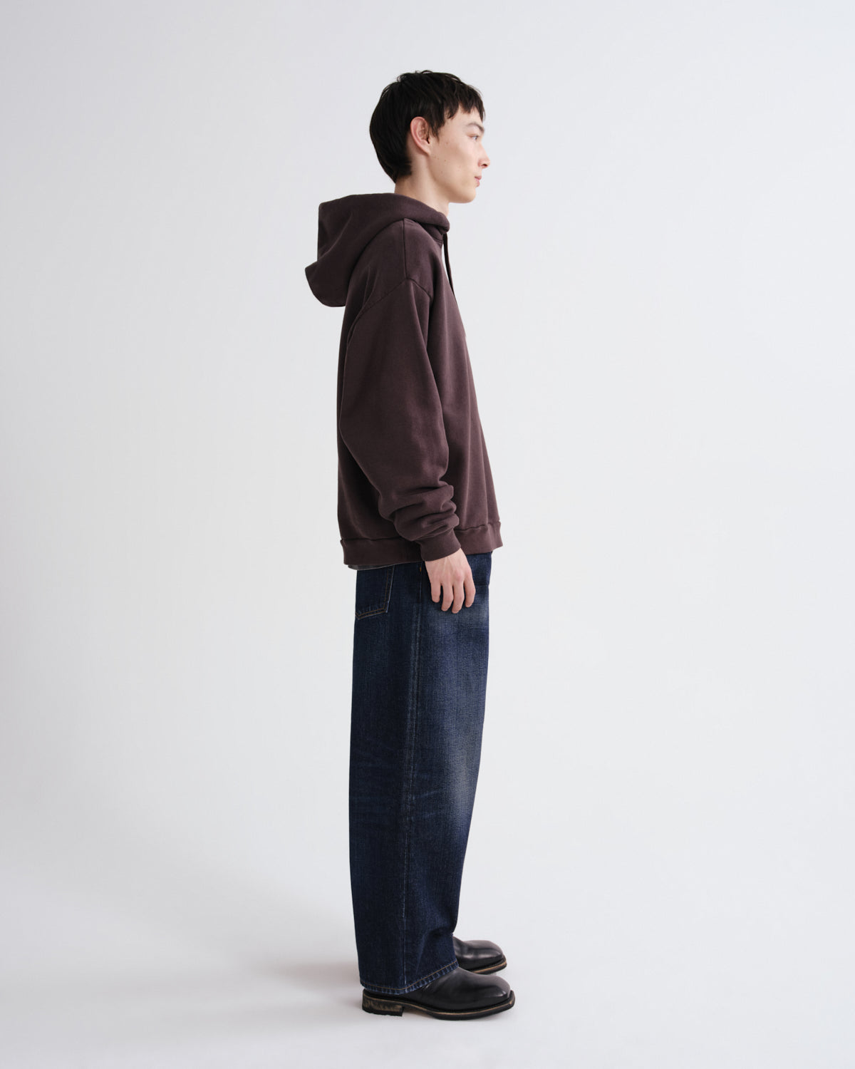 Person wearing a brown hoodie and blue jeans standing against a white background
