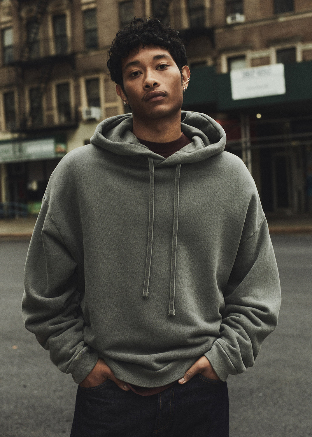 Man wearing a gray hoodie standing on a street with buildings in the background