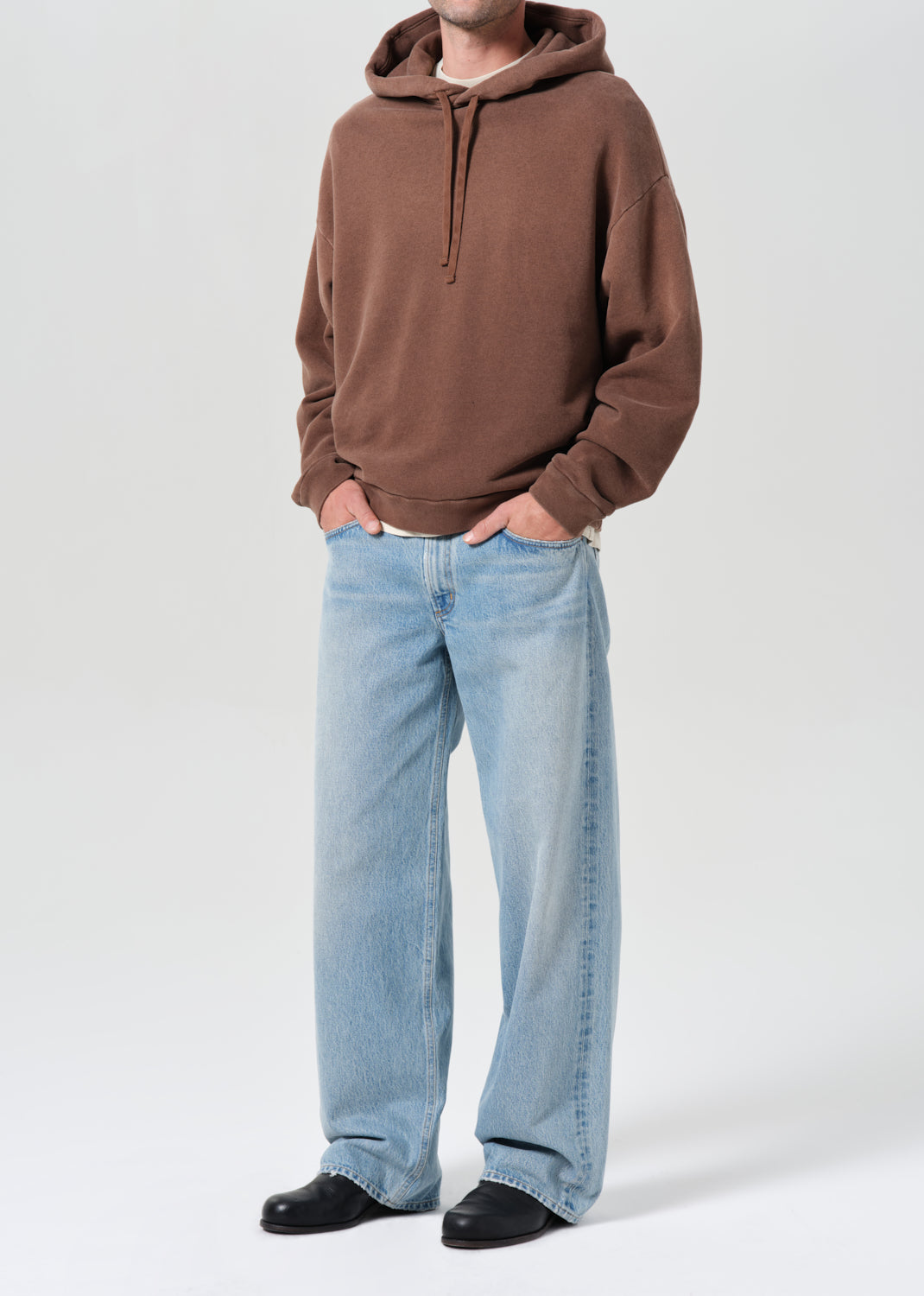 Person wearing a brown hoodie and light blue jeans on a white background