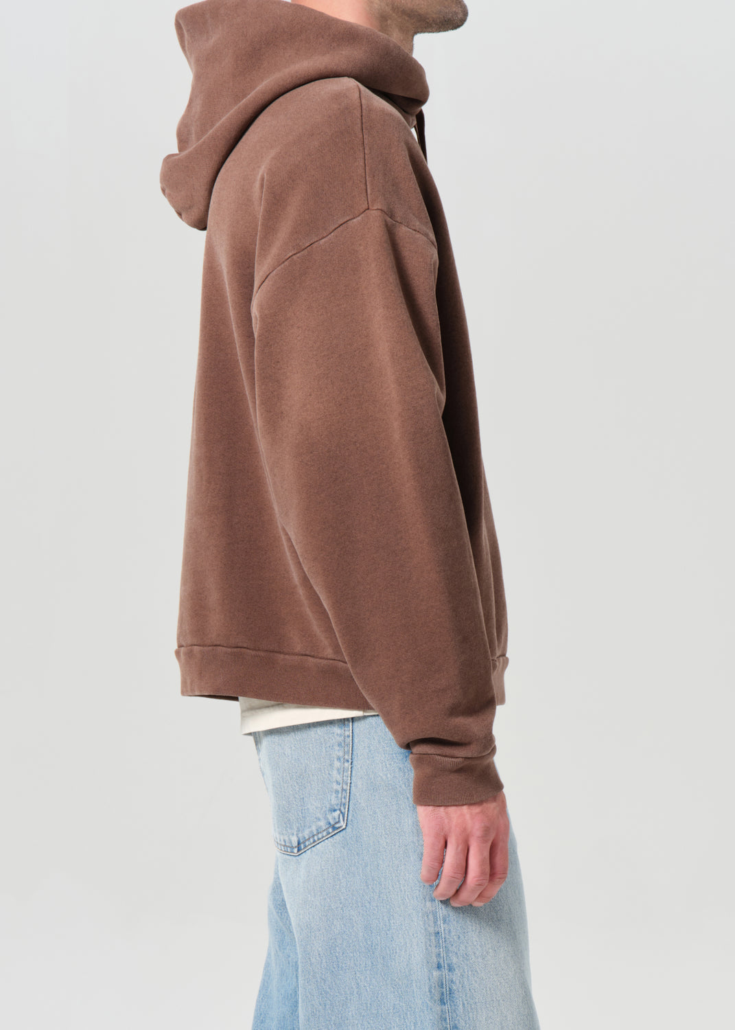 Person wearing a brown hoodie and light blue jeans on a plain background