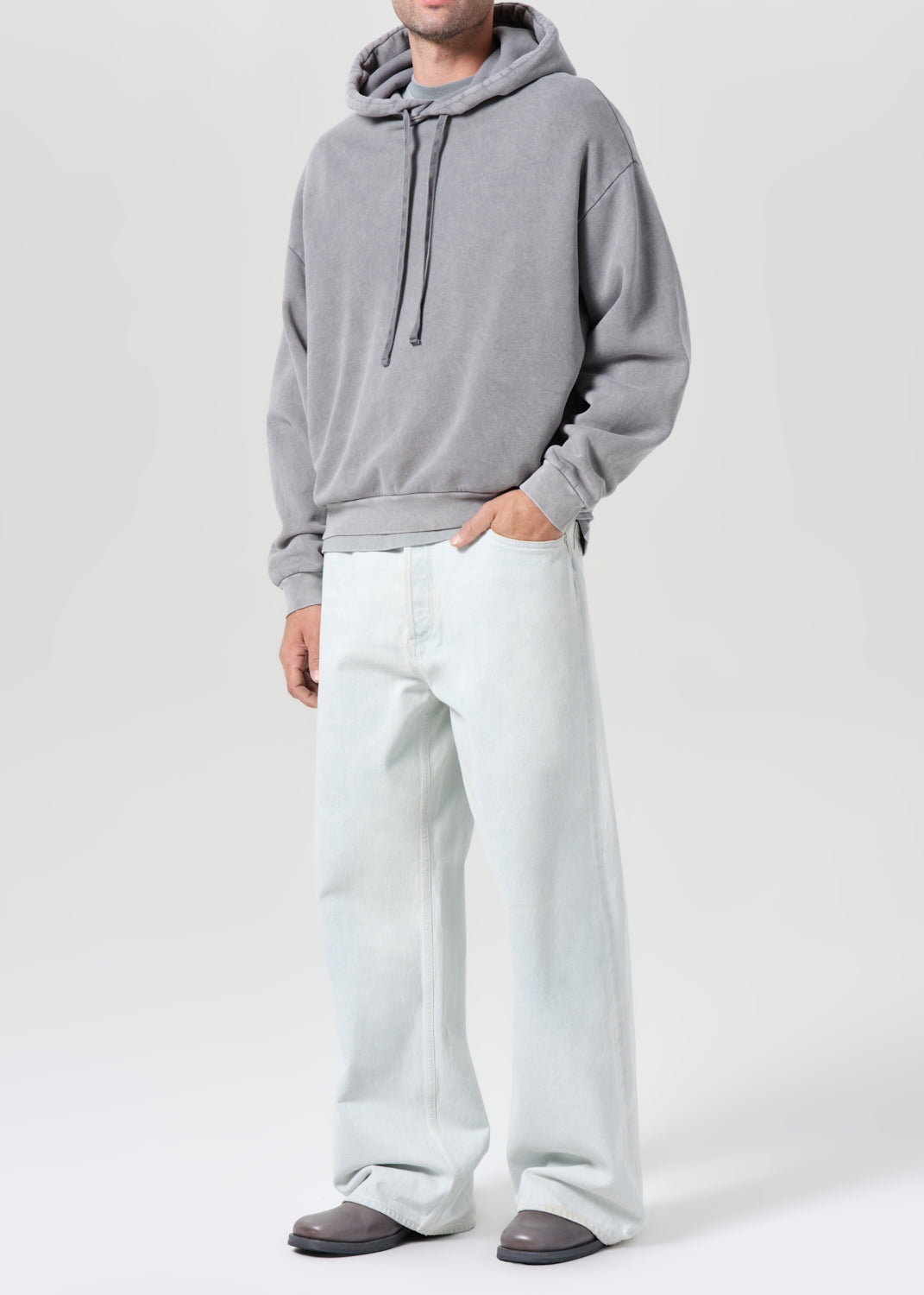 Person wearing a gray hoodie and white pants on a white background