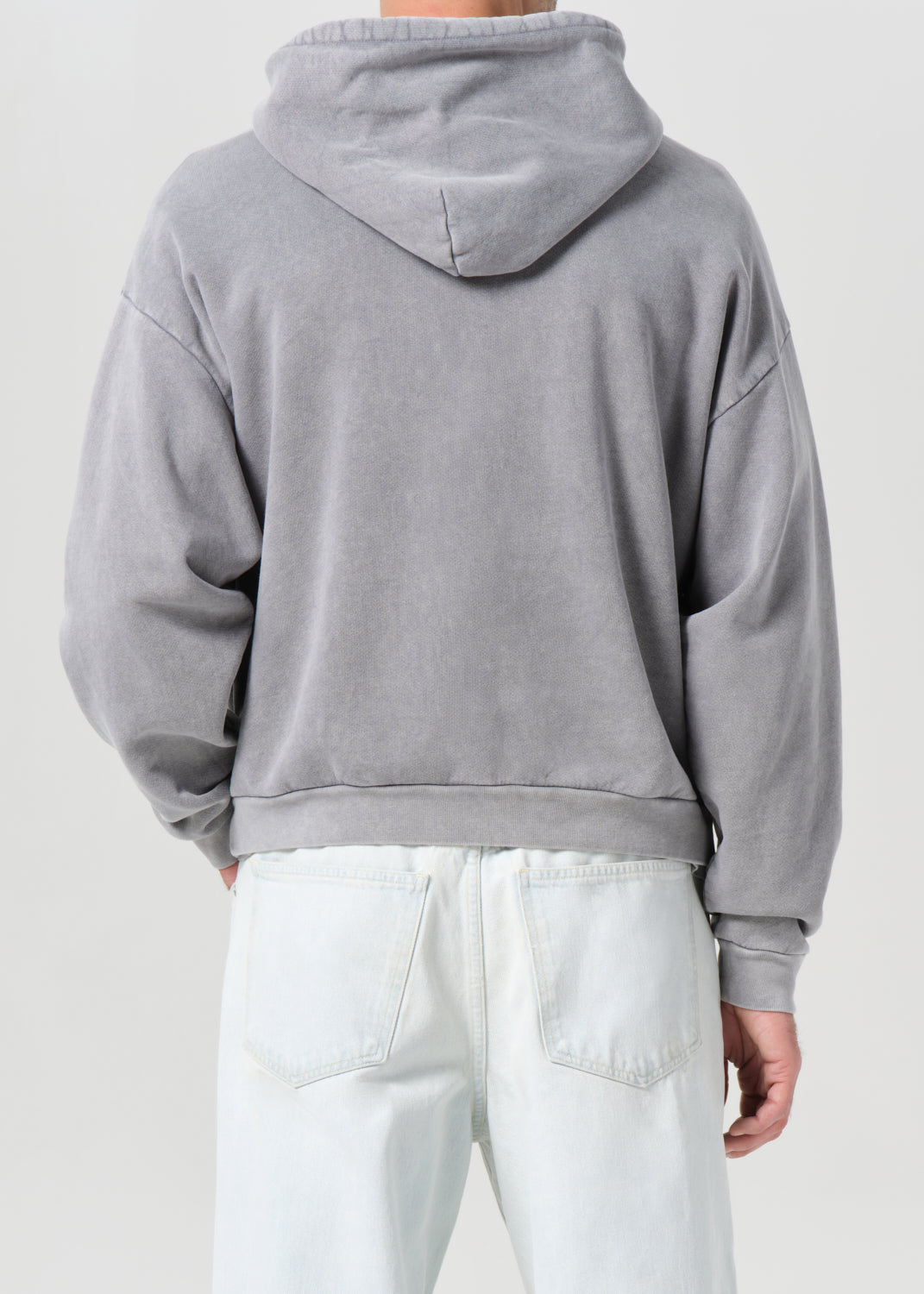 Person wearing a gray hoodie and white pants on a light gray background