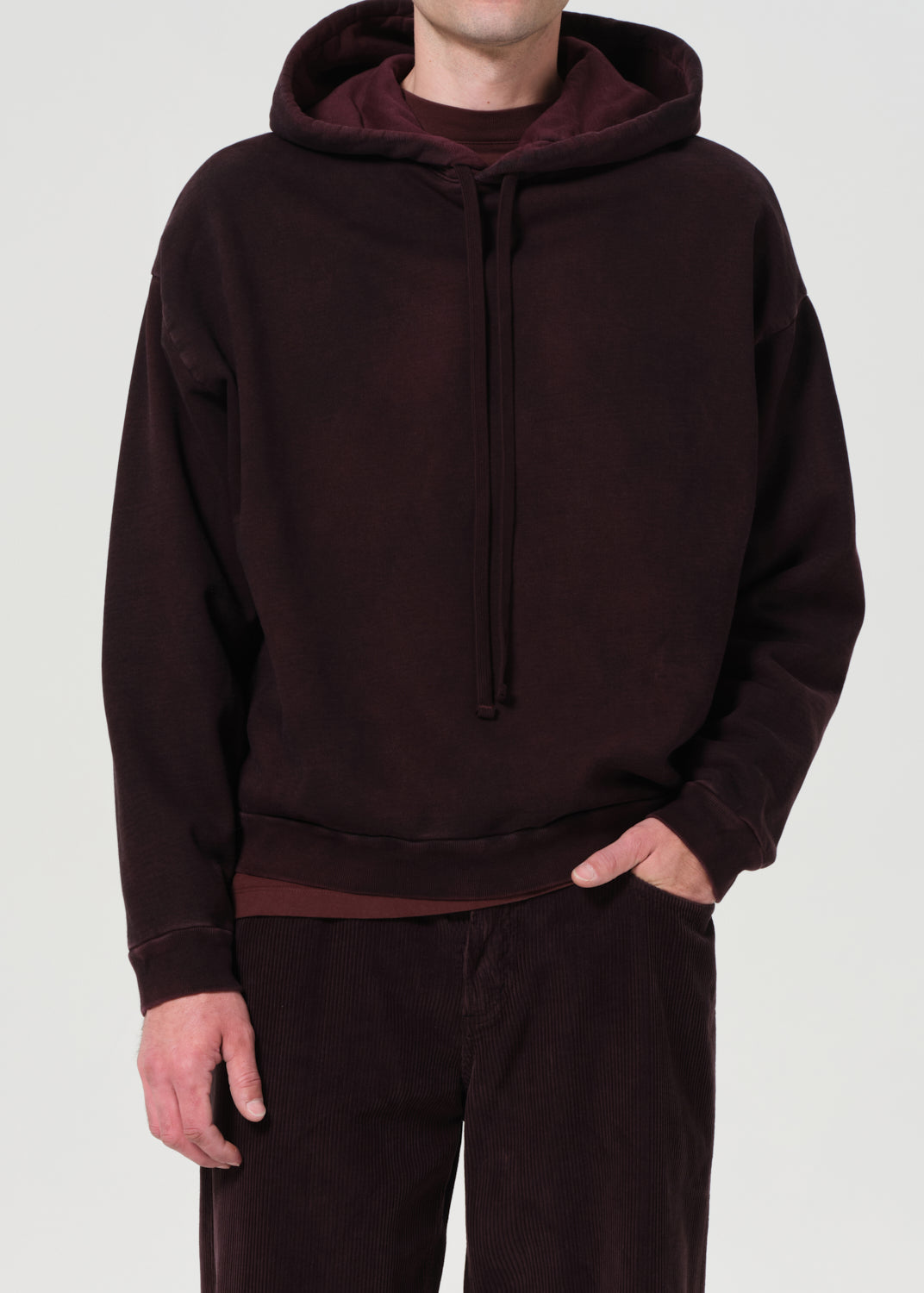 Person wearing a dark brown hoodie and pants on a light gray background