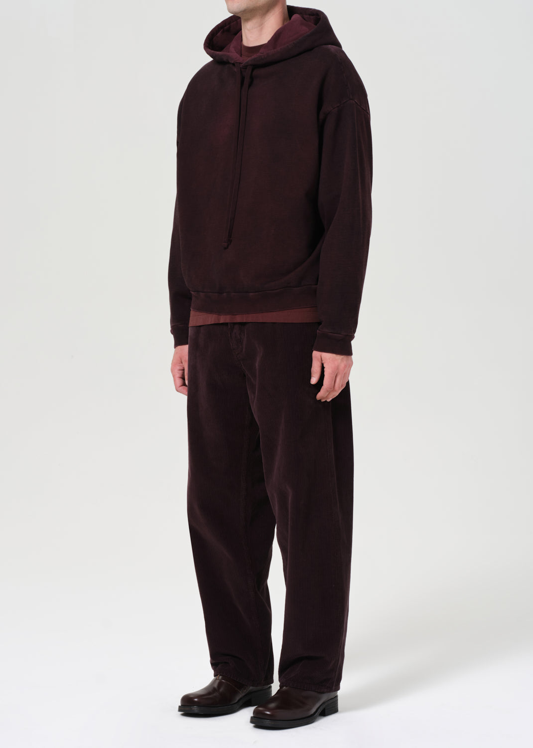 Person wearing a dark brown hoodie and pants on a white background
