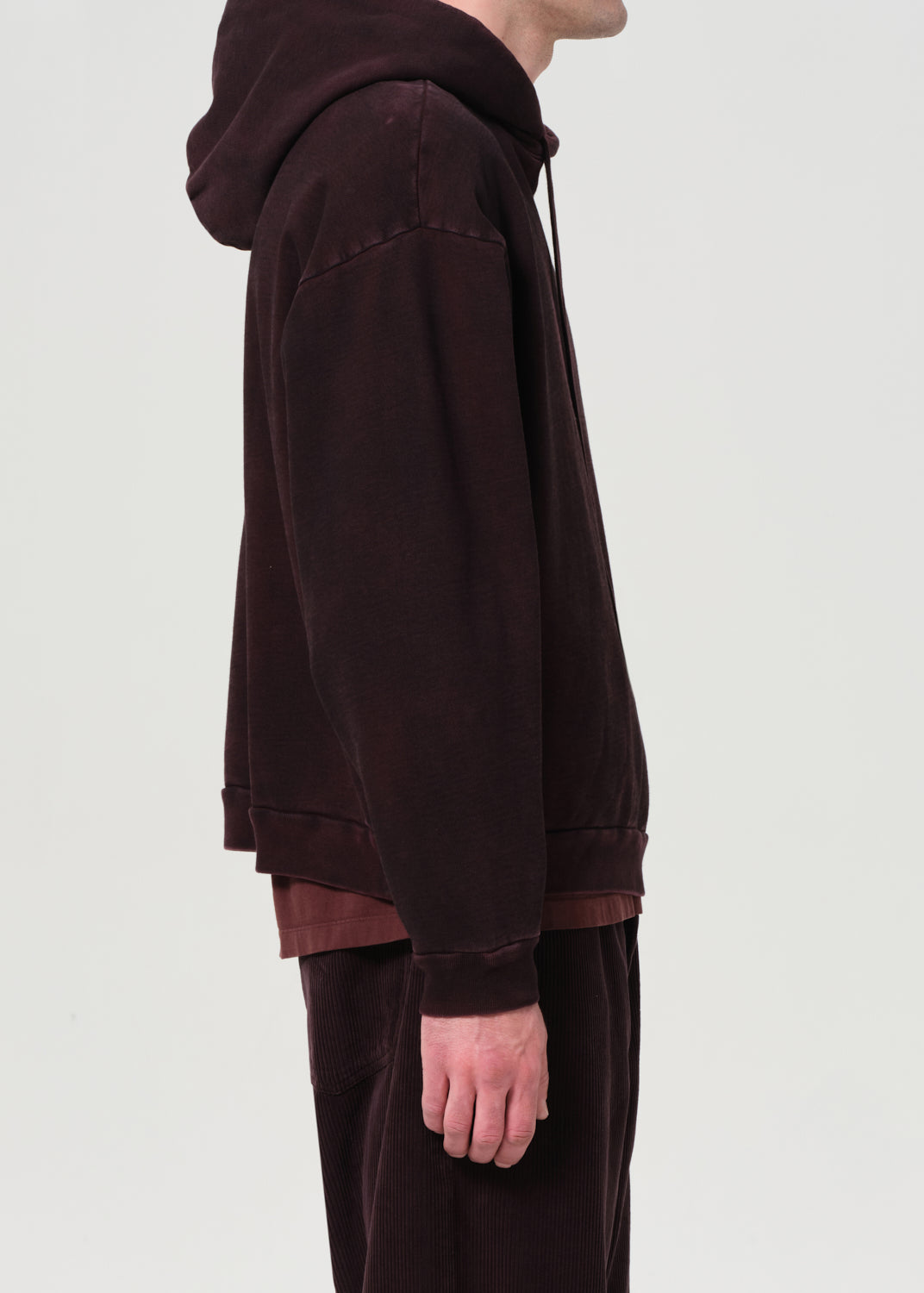 Person wearing a dark brown hoodie and pants on a light gray background