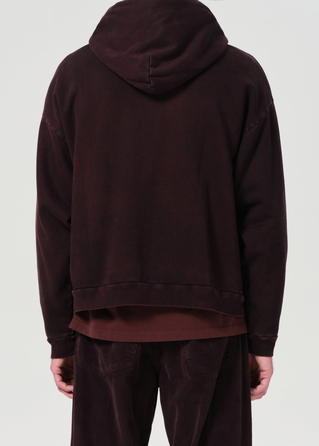 Person wearing a dark brown hoodie and pants on a light gray background
