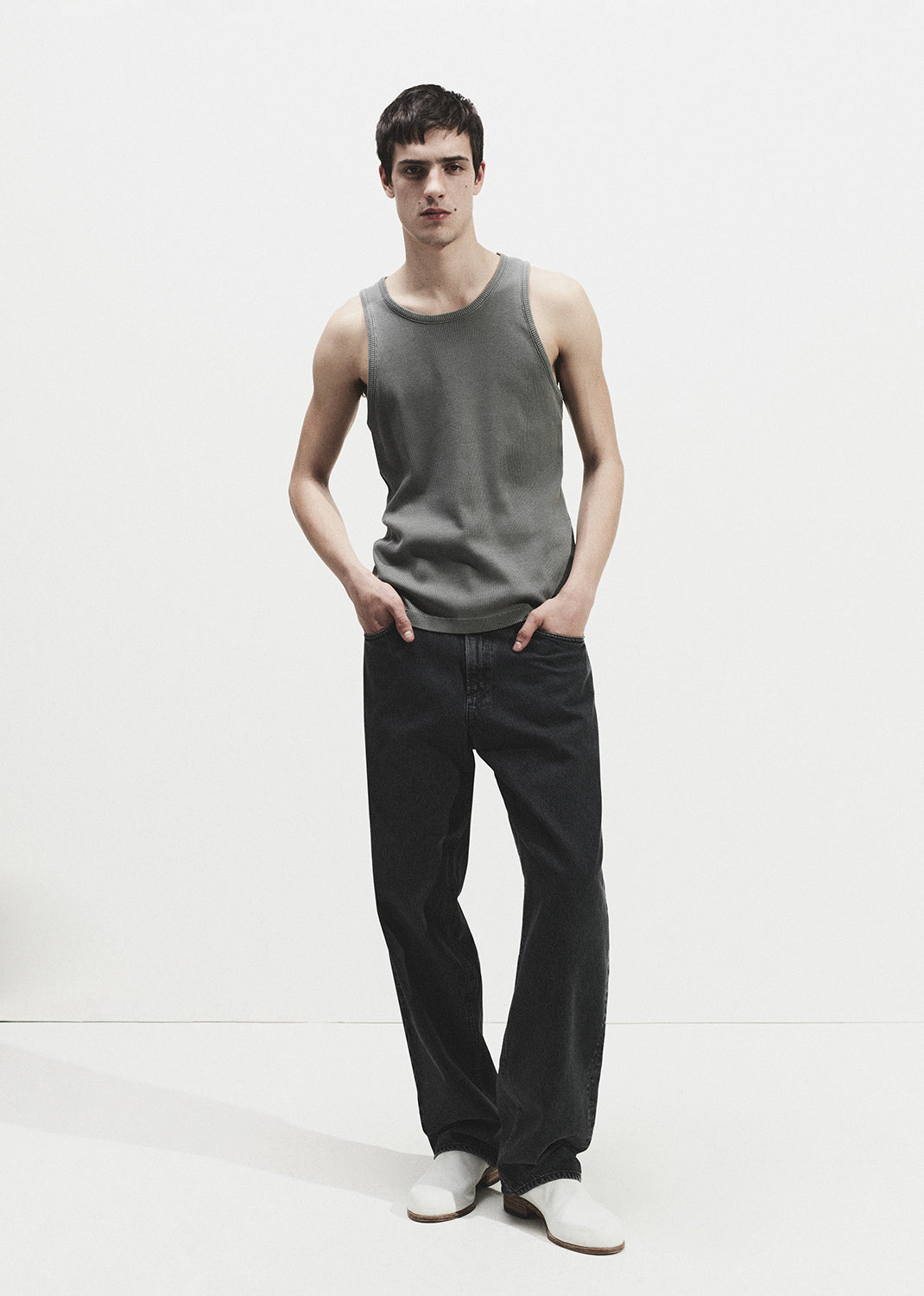 Man wearing a grey tank top and black pants on a grey background