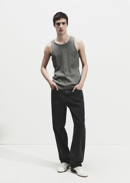 Man wearing a grey tank top and black pants on a grey background