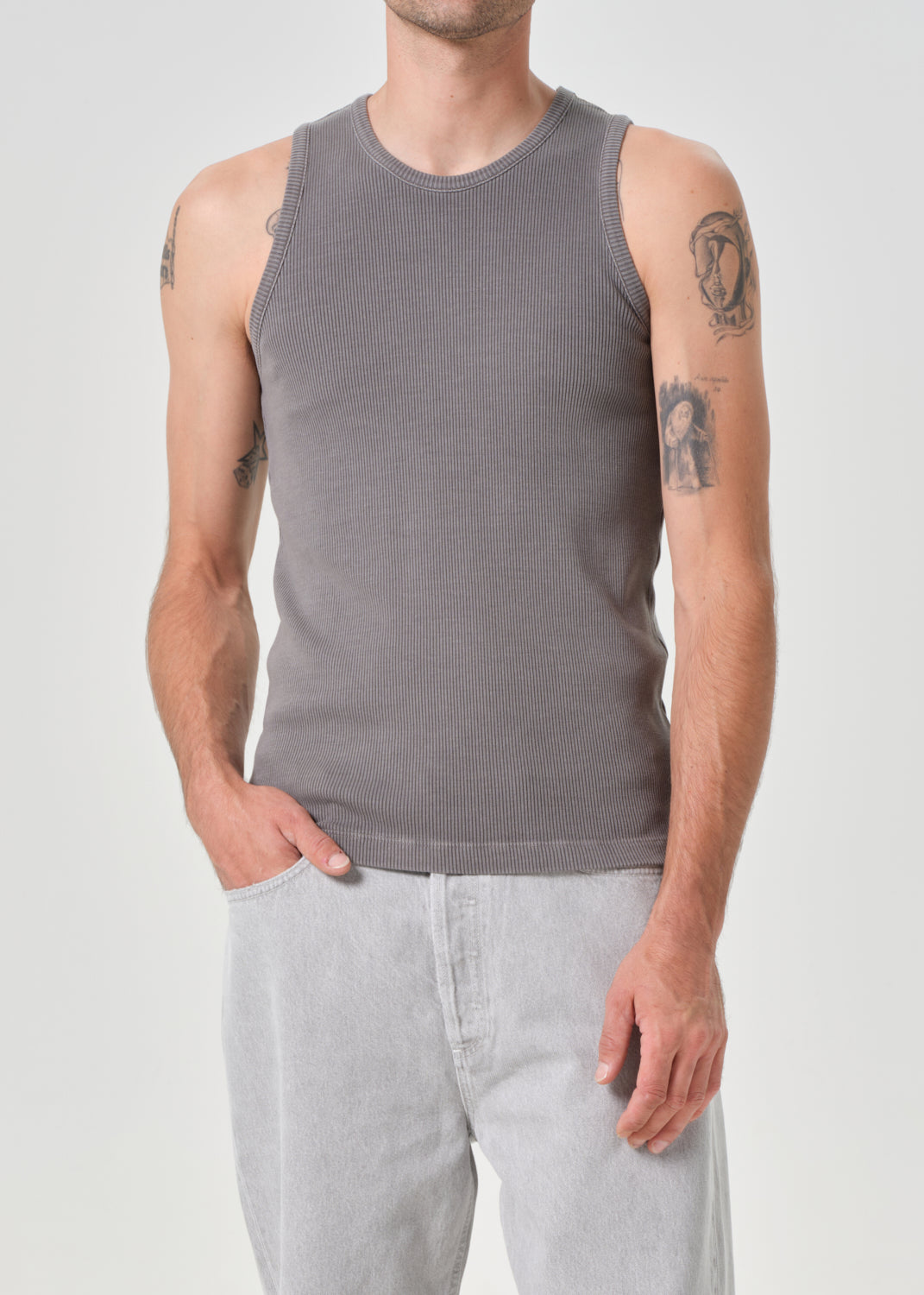 Person wearing a grey tank top and light grey pants on a grey background