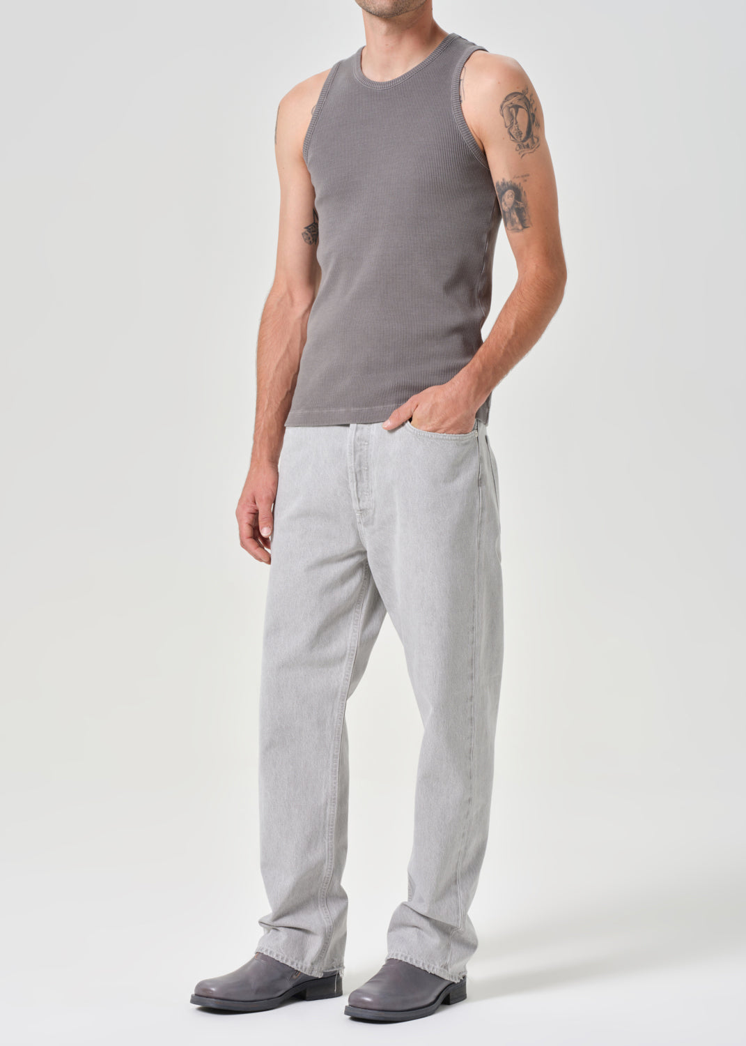 Man wearing a grey sleeveless shirt and light grey pants on a grey background