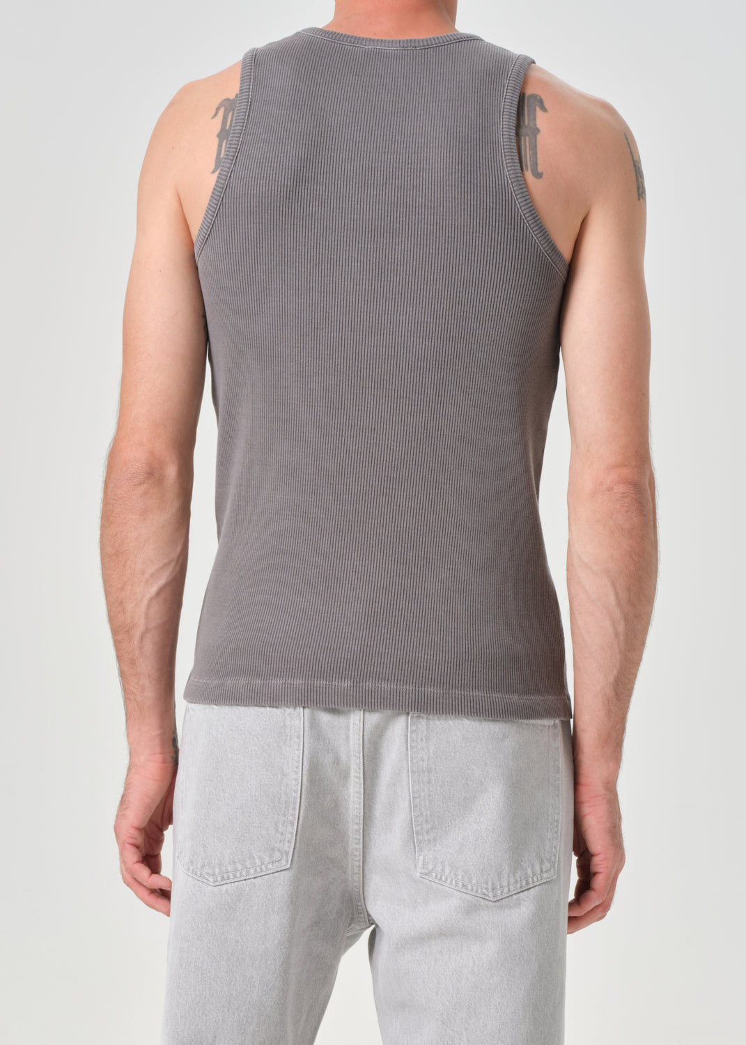 Person wearing a grey tank top and light grey pants on a grey background