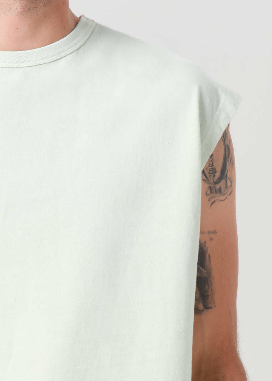 Person wearing a light gray t-shirt with tattoos on the arm against a white background