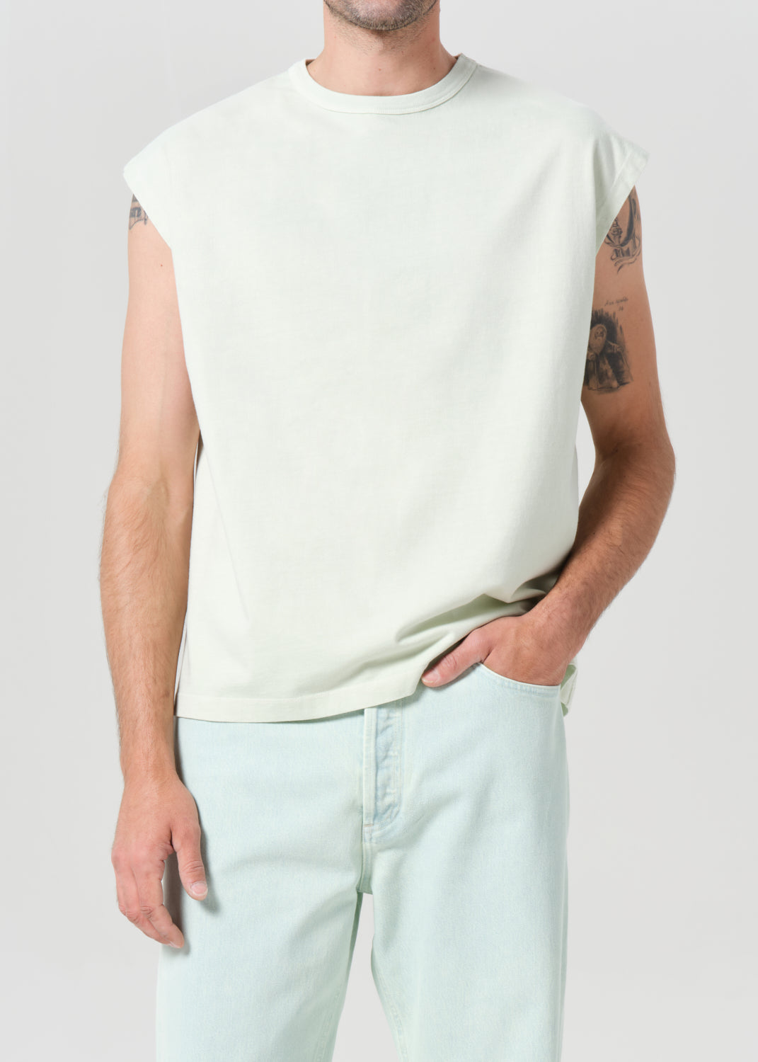 Person wearing a plain white sleeveless shirt and light blue jeans on a white background