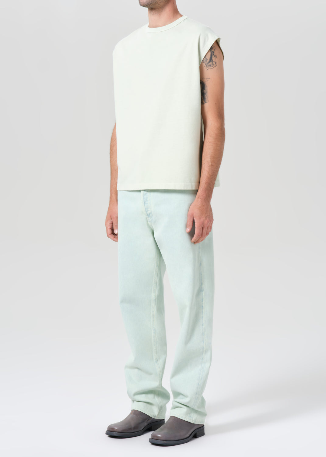 Person wearing a sleeveless light green top and light blue pants on a white background