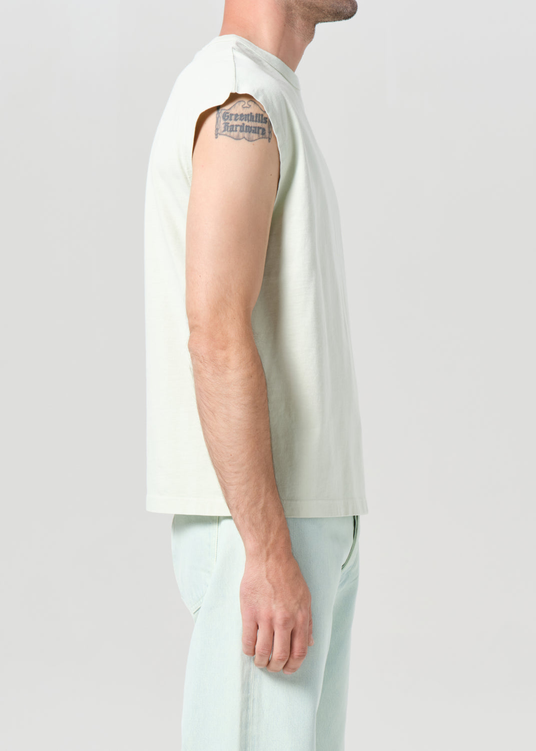 Person wearing a white sleeveless shirt and light-colored pants on a plain background