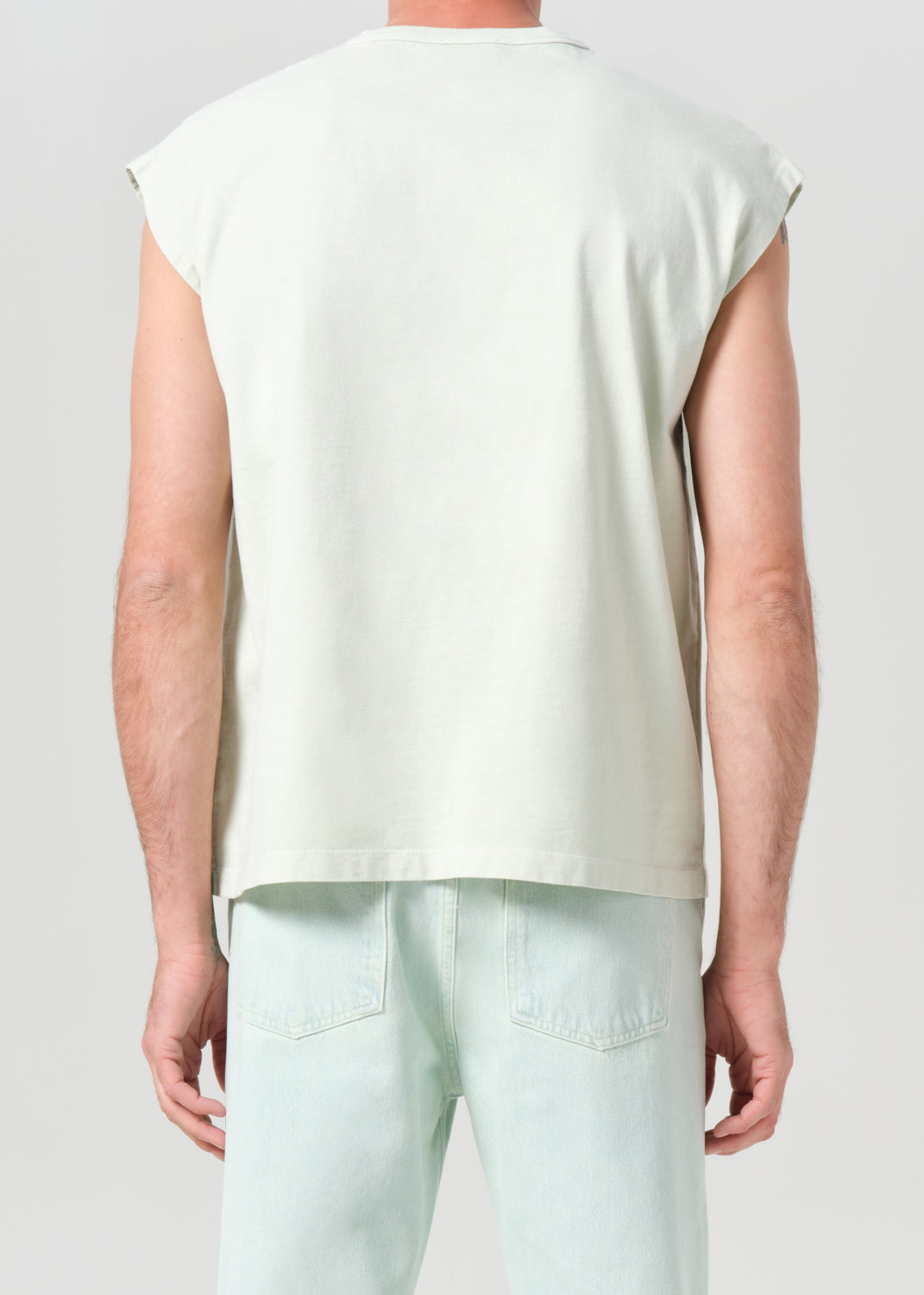 Person wearing a light green sleeveless top and light blue pants on a plain background