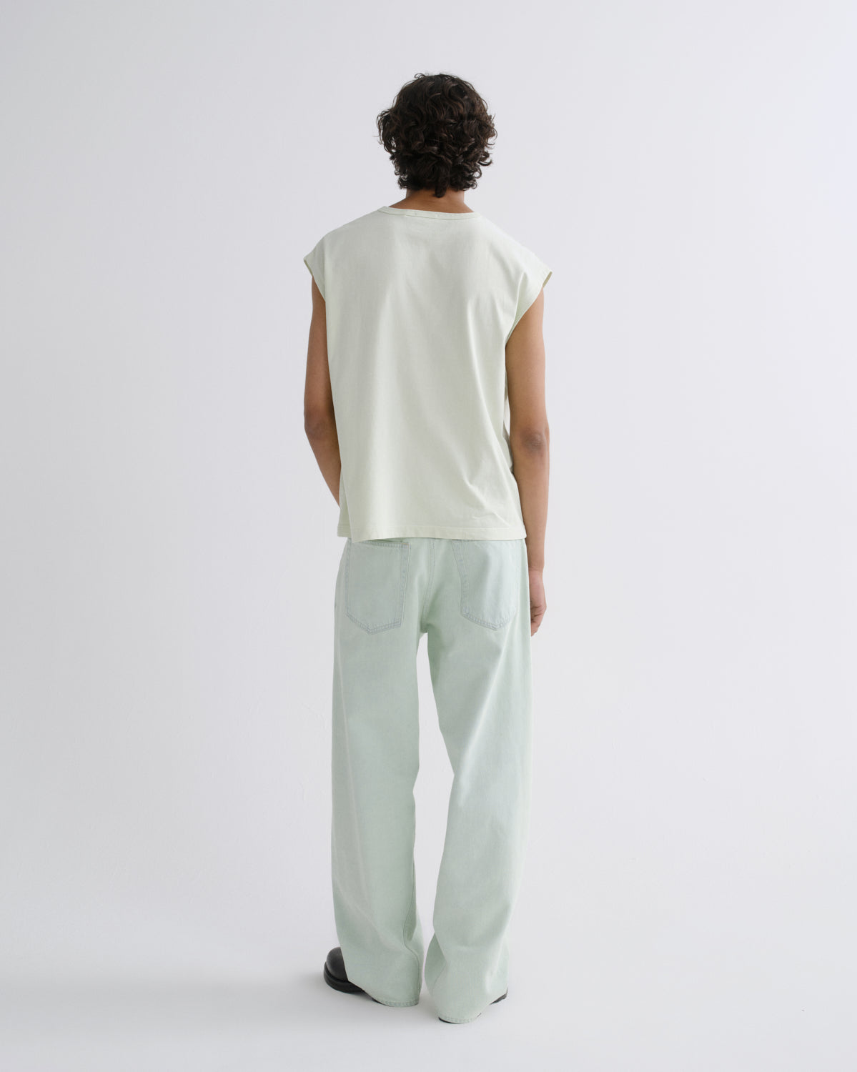 A model shown from the back wearing a light sage green sleeveless t-shirt and matching wide-leg trousers against a plain white studio background.