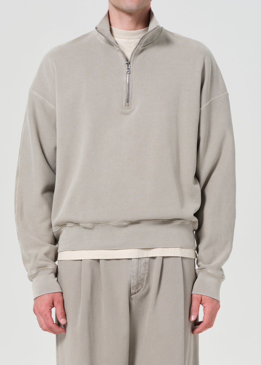 Person wearing a beige half-zip sweatshirt and pants on a white background