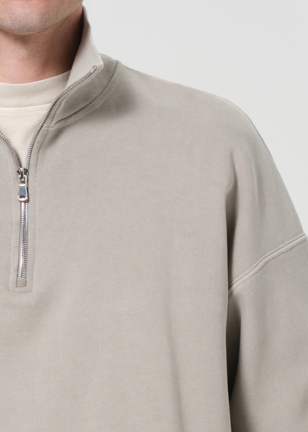Close-up of a beige pullover with a quarter zip and zipper detail on a light gray background