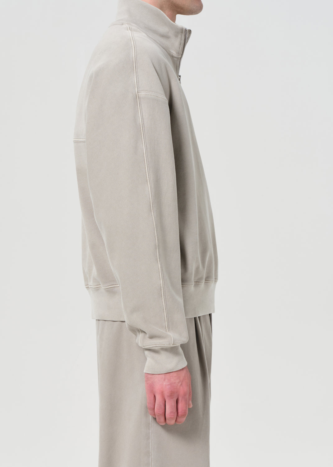 Person wearing a beige tracksuit with a plain background