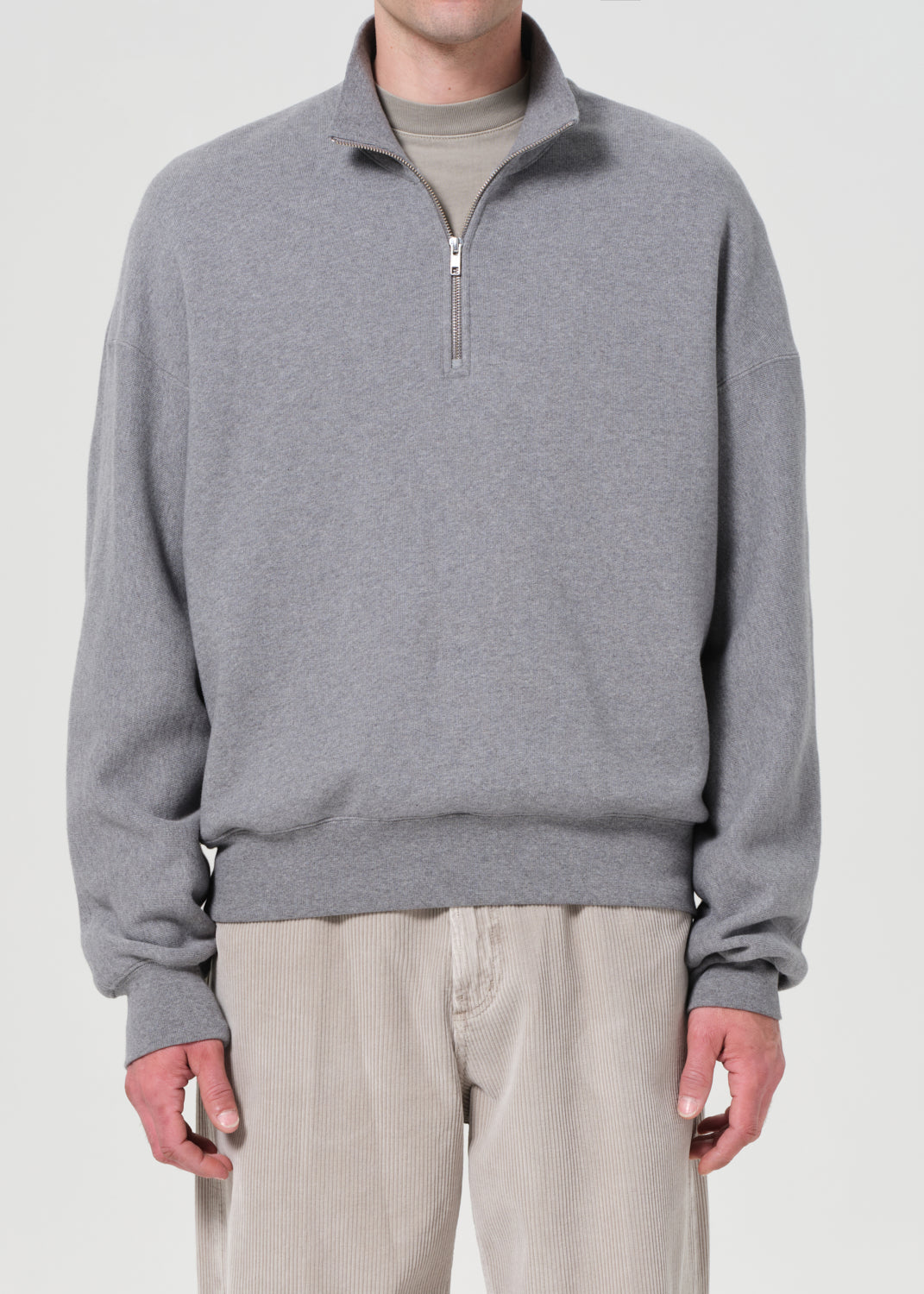Person wearing a gray half-zip sweatshirt and light-colored pants on a white background