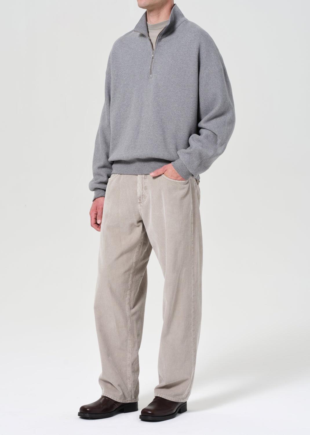 Person wearing a gray sweater and beige pants on a white background