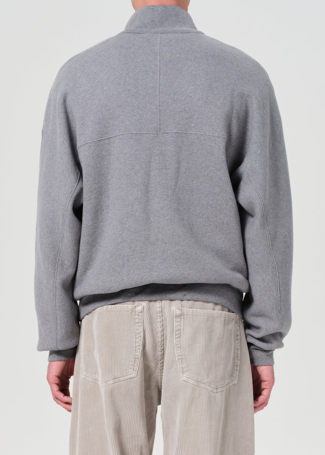 Person wearing a gray sweater and beige pants on a plain background