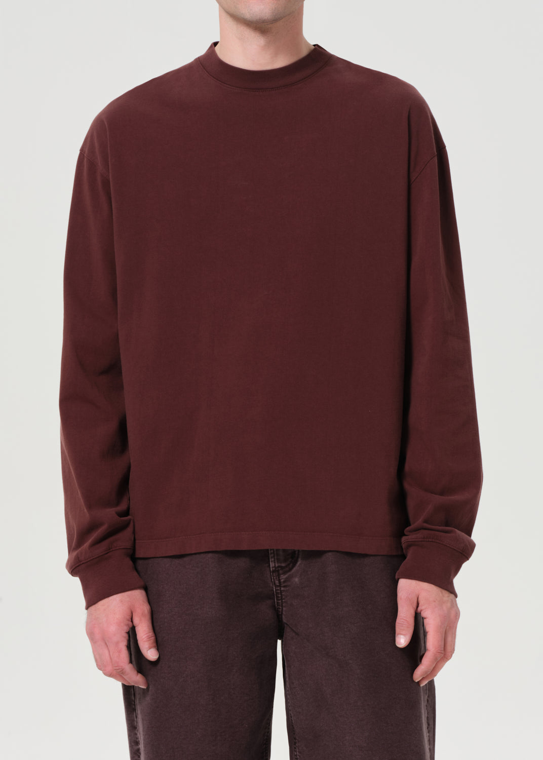 Person wearing a brown long-sleeve shirt and dark pants on a white background