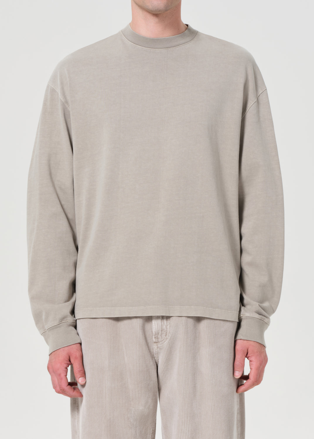 Person wearing a beige long-sleeve shirt and pants on a white background