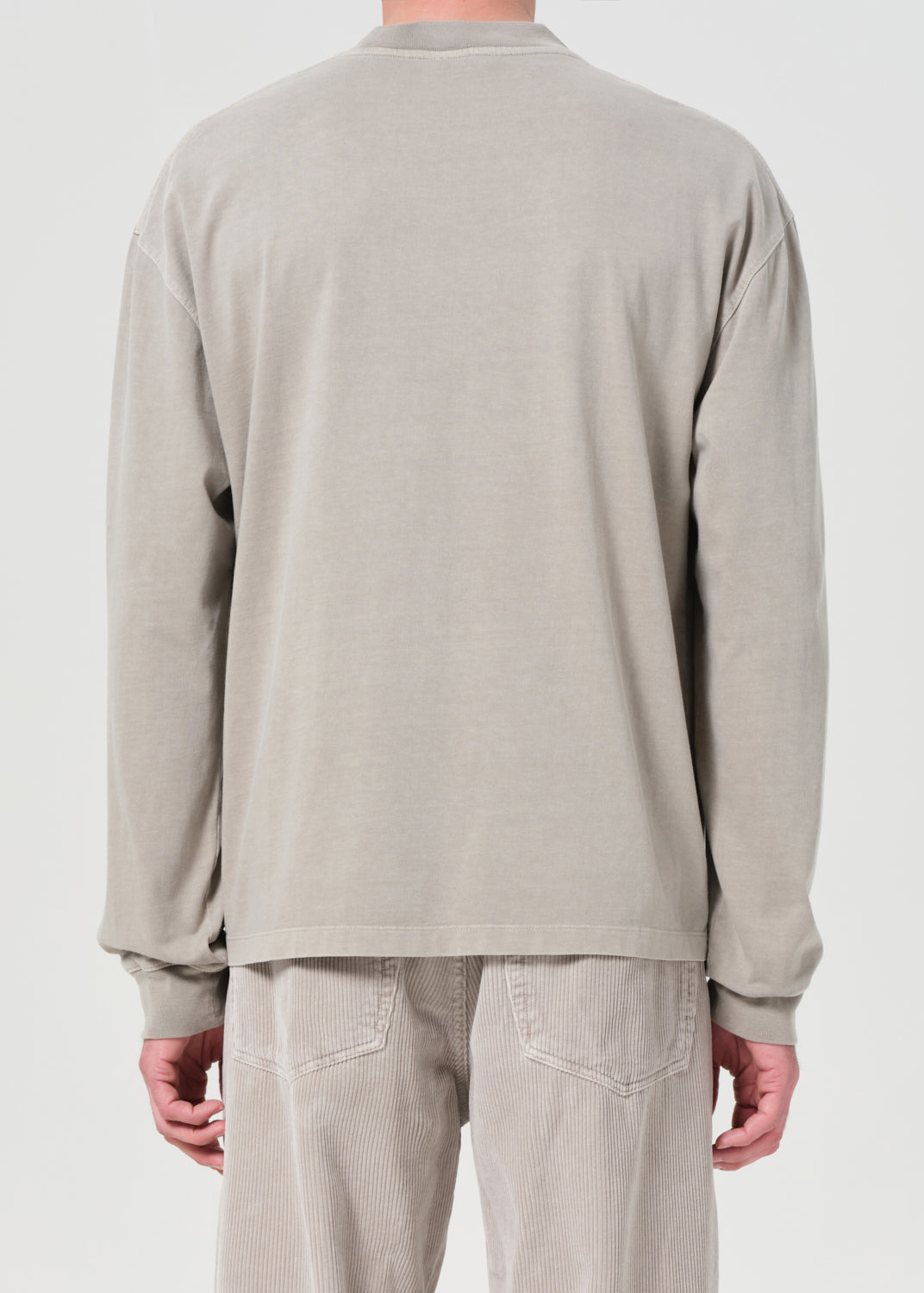 Person wearing a beige long-sleeve shirt and pants on a white background