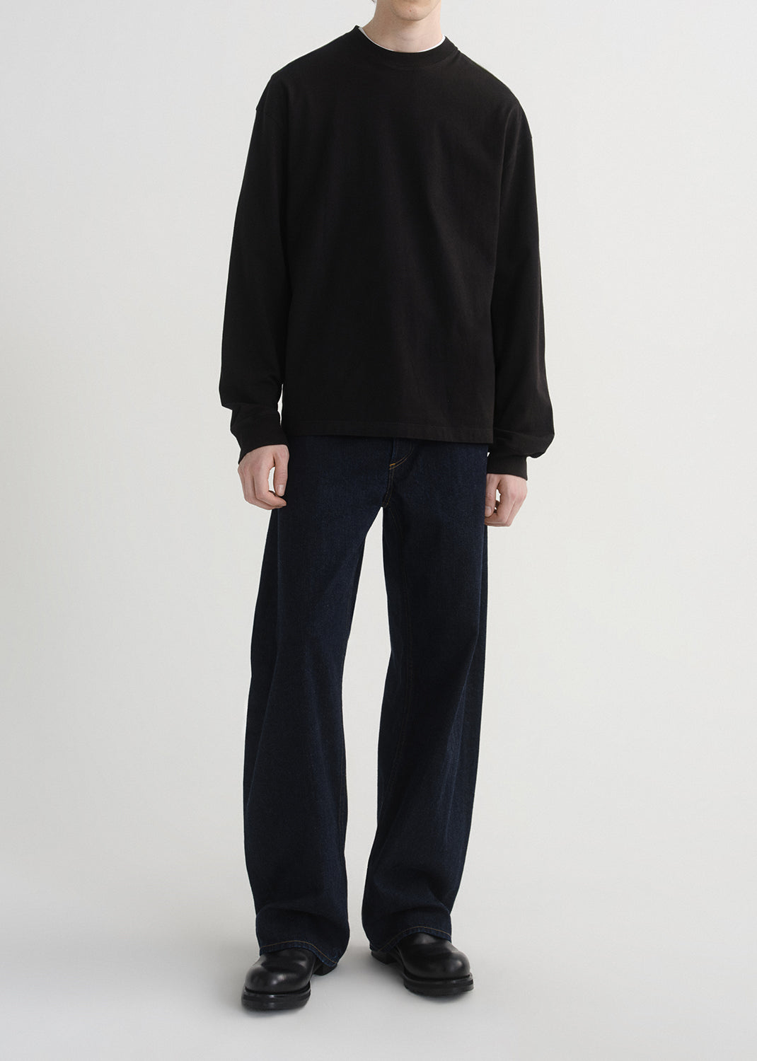 Person wearing a black long-sleeve shirt and black pants on a grey background