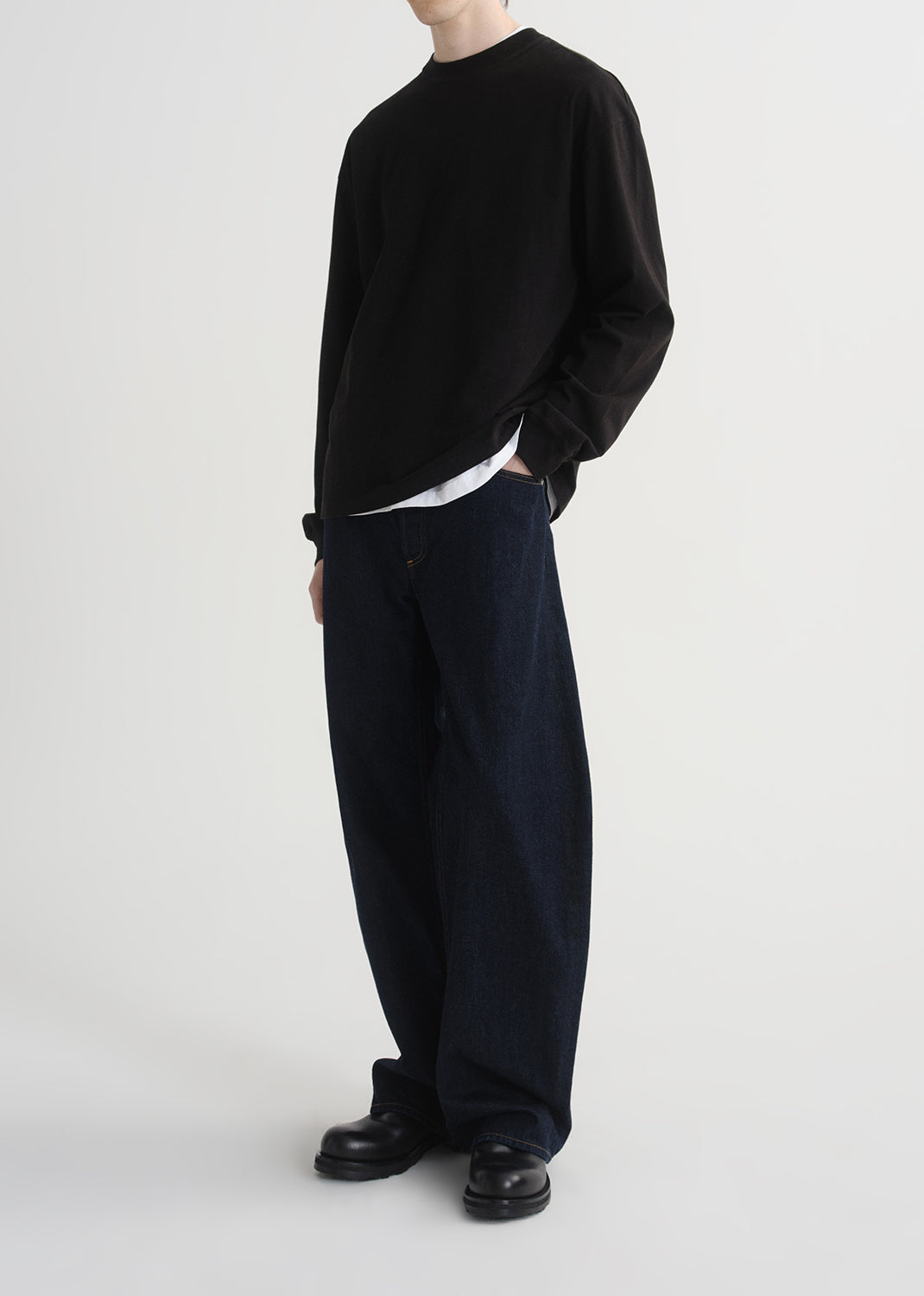 Person wearing a black sweater and dark pants on a grey background