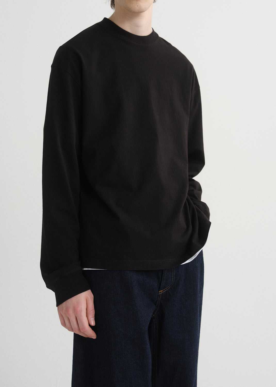 Person wearing a black sweatshirt and dark pants on a grey  background