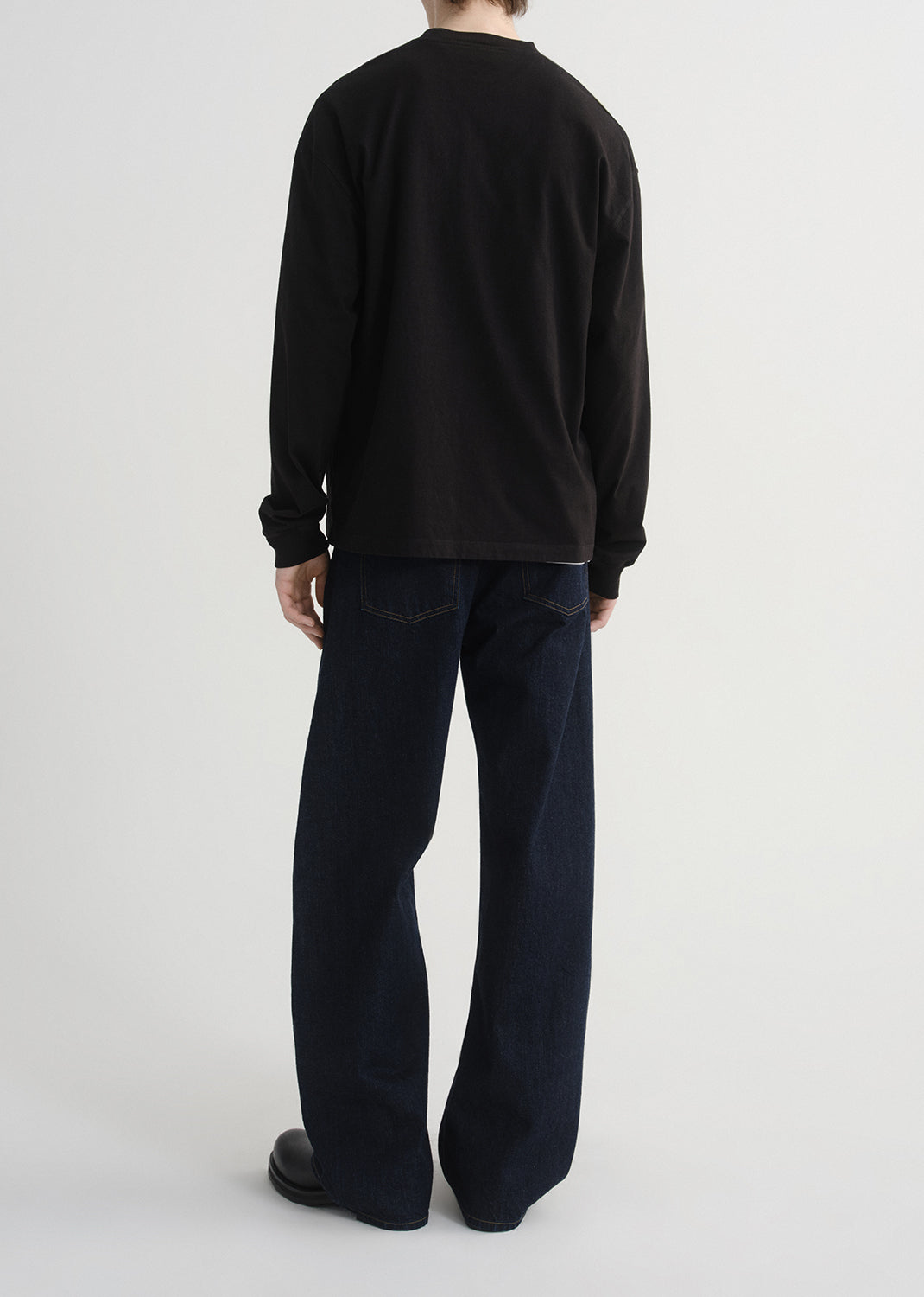 Person wearing a black long-sleeve shirt and dark pants on a grey background