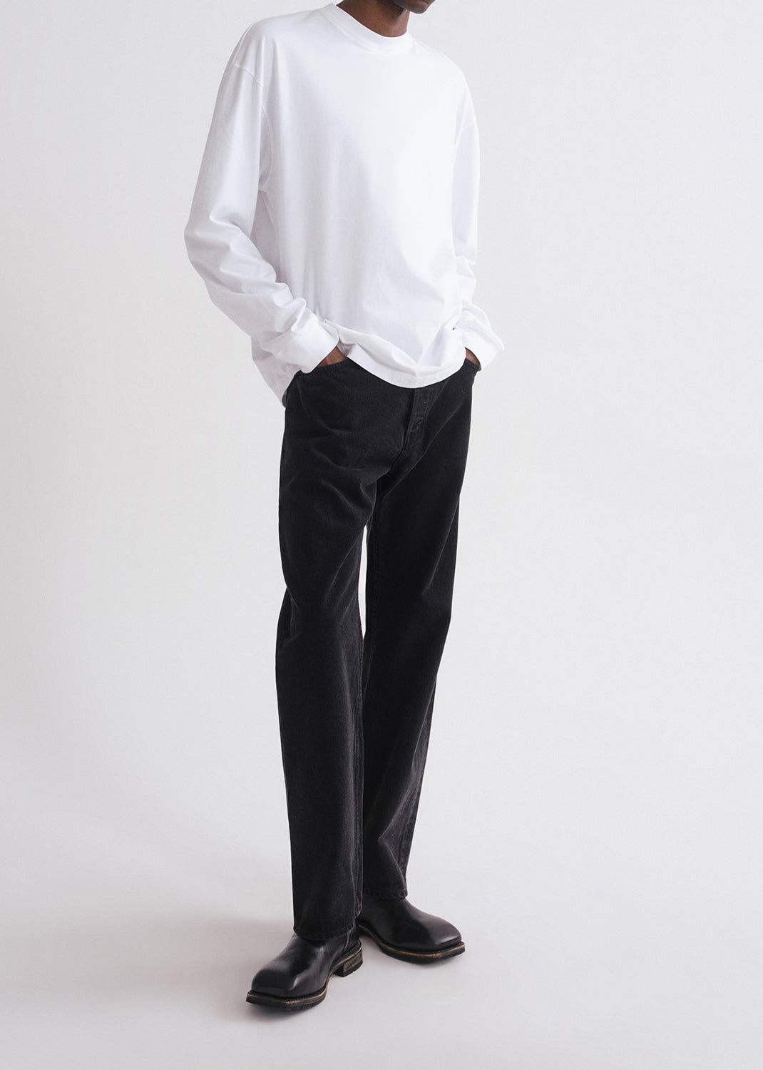 Person wearing a white sweater and black pants on a grey background