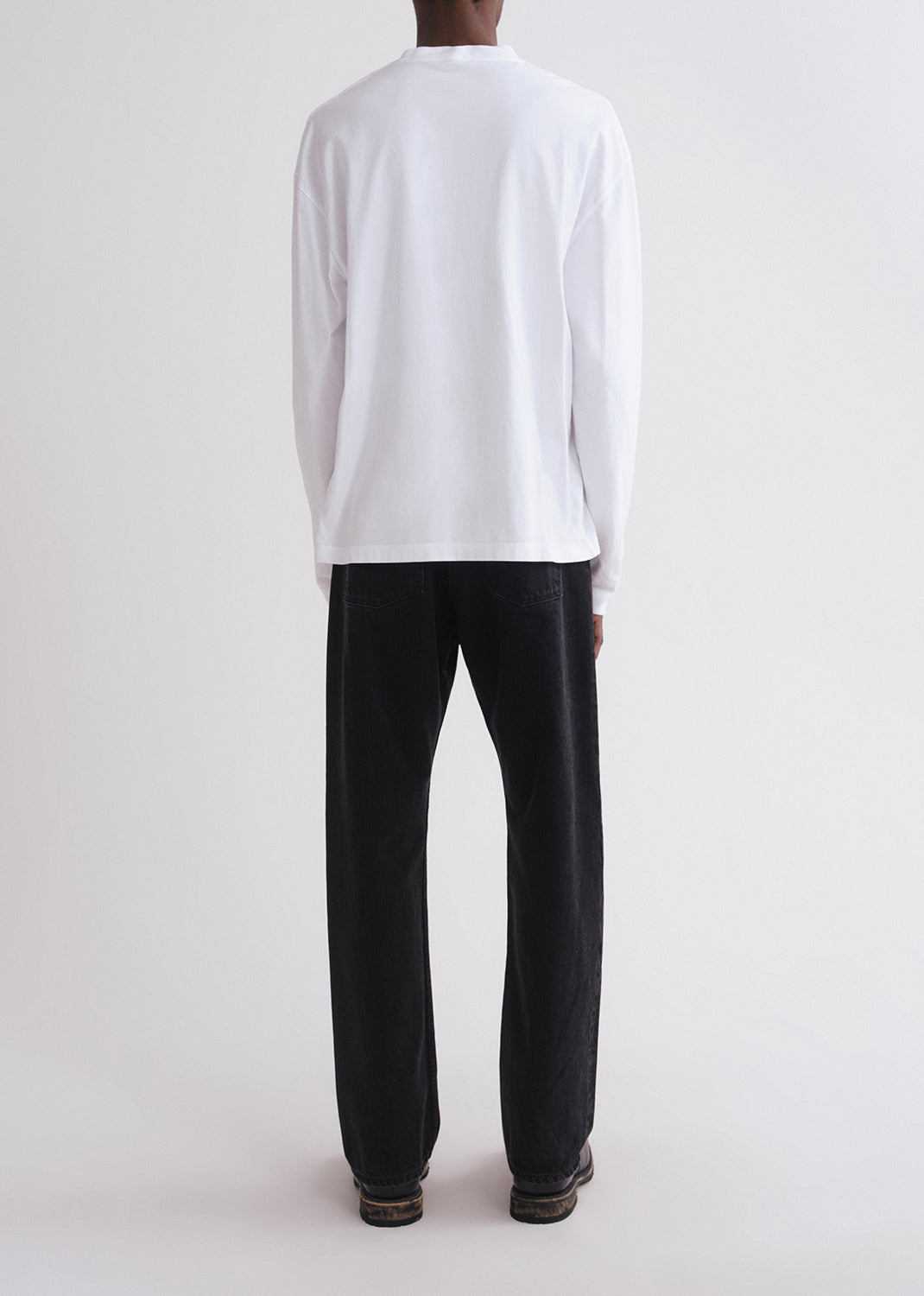 Person wearing a white long-sleeve shirt and black pants on a grey background