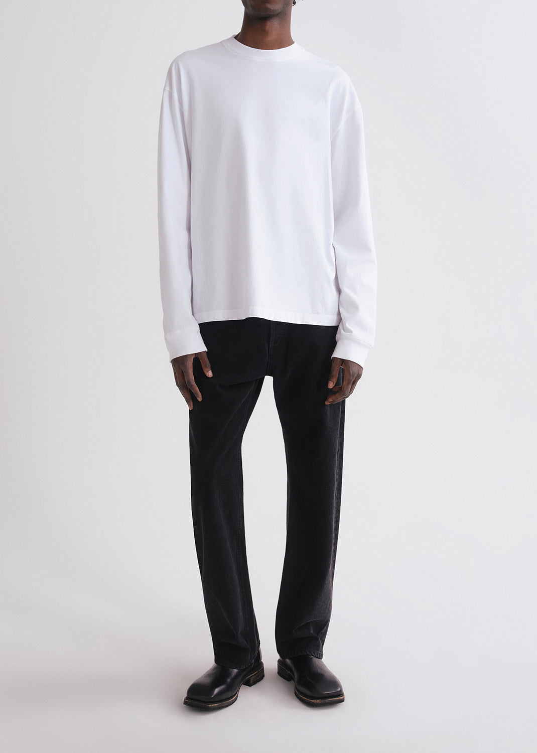 Person wearing a white long-sleeve shirt and black pants on a grey background