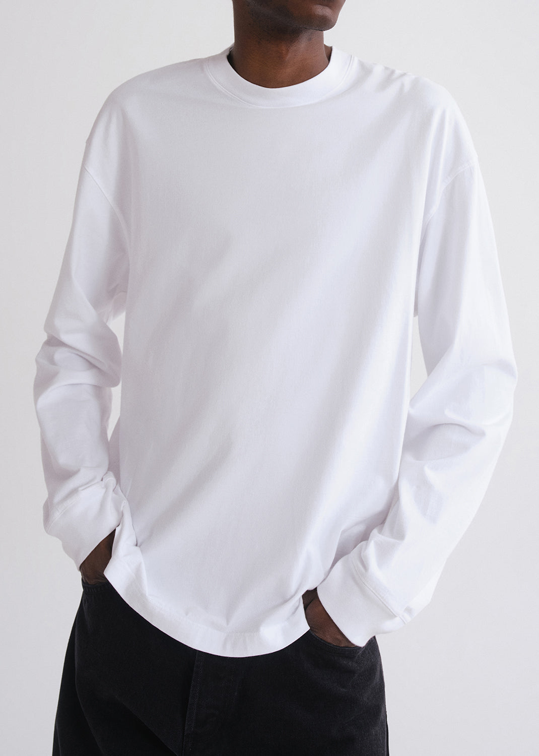 Person wearing a plain white long-sleeve shirt against a grey background
