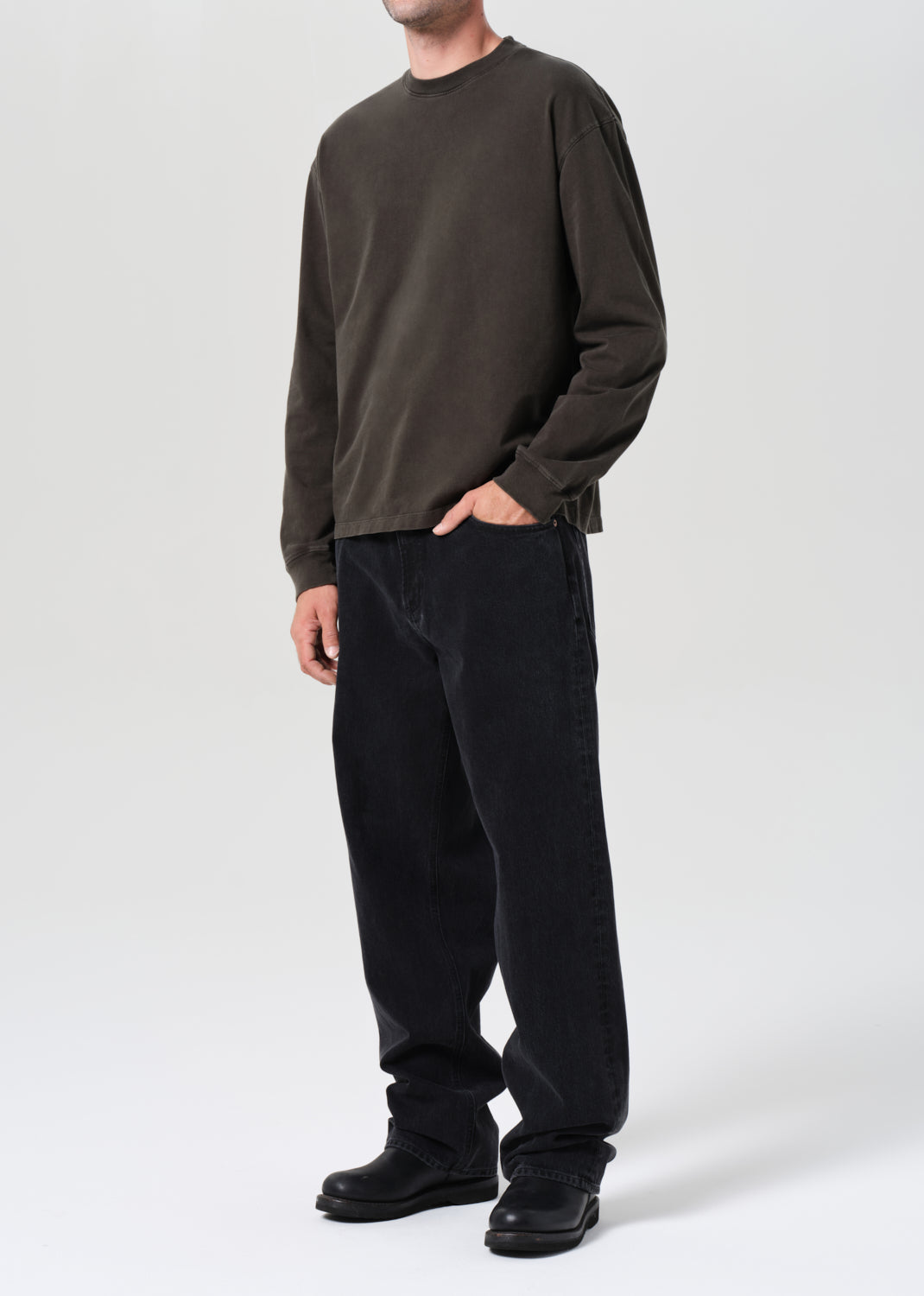 Person wearing a dark brown long-sleeve shirt and black pants on a white background