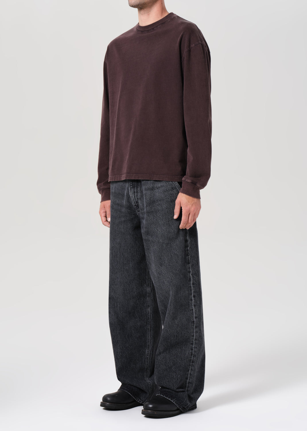 Person wearing a brown long-sleeve shirt and dark jeans on a white background