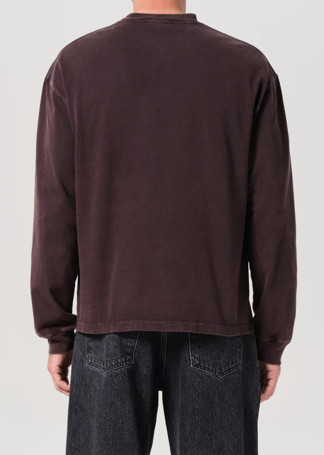 Person wearing a dark brown long-sleeve shirt and dark jeans on a light gray background